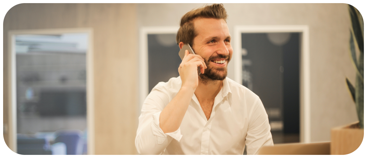 Photographie d'un homme barbu et souriant, en chemise blanche, manches remontées, qui téléphone dans un environnement de bureau.