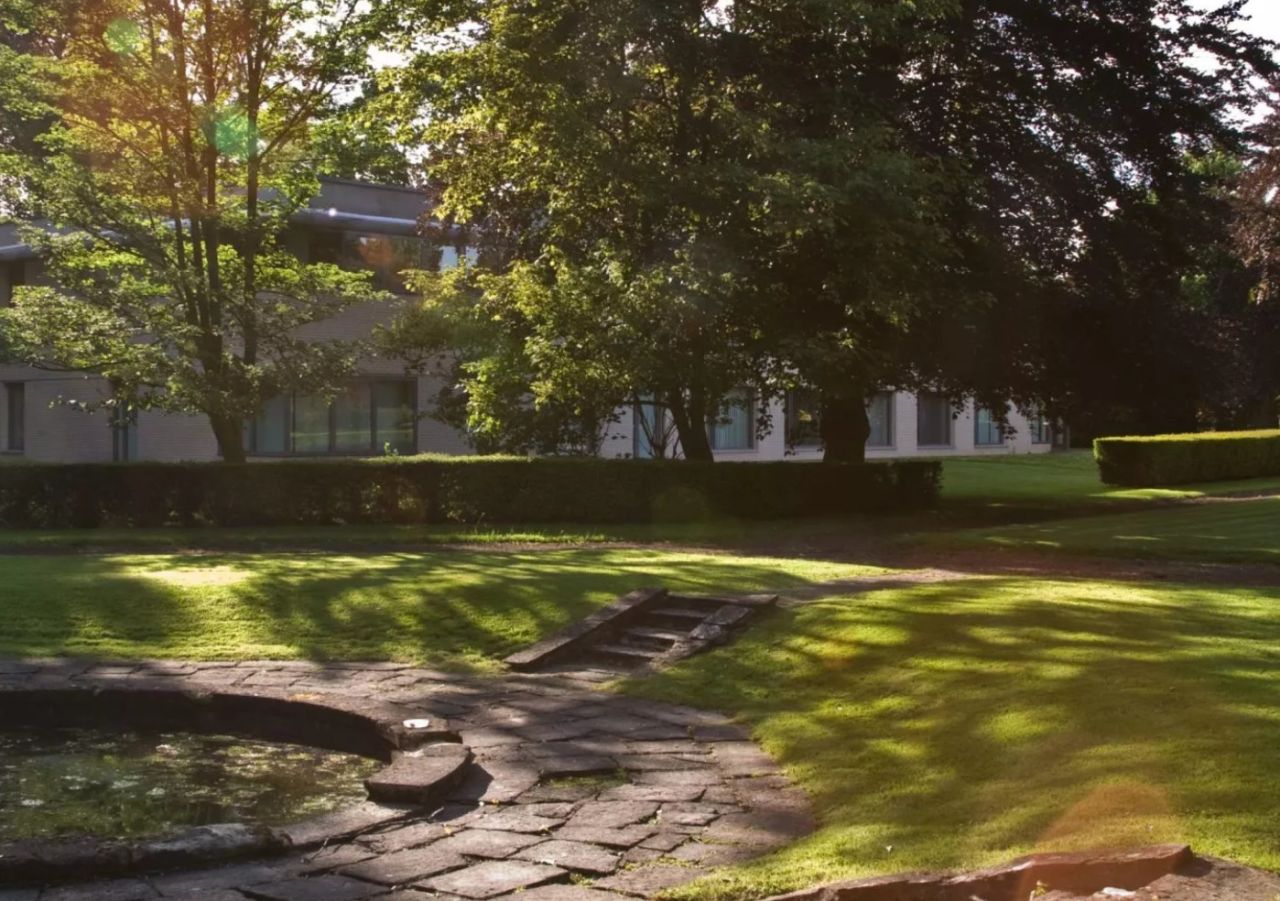 Photographie d'un espace vert, entouré de bâtiments en partie dissimulés par des arbres et représentant une vue attrayante du parc du campus CPA à Lille.