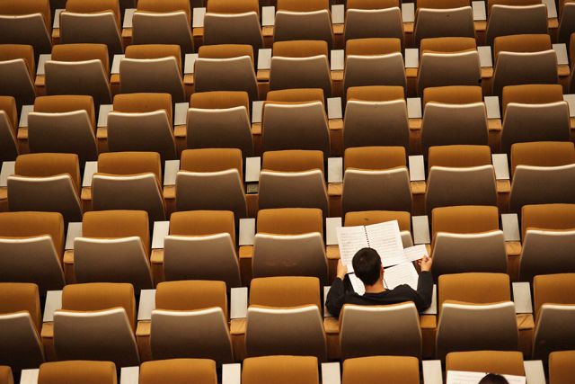 Photographie d'un amphithéâtre avec une seule personne assise et qui travaille, illustrant le financement de la formation pour les personnes méritantes et qui n'ont pas les moyens financiers pour le faire.